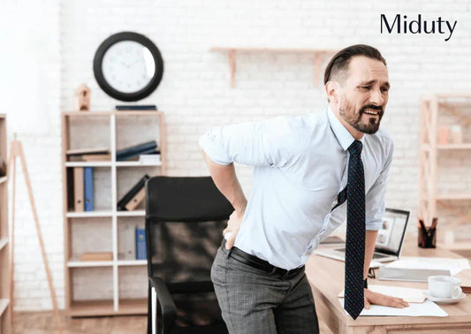 Man holding his lower back in pain while standing at a desk in an office setting