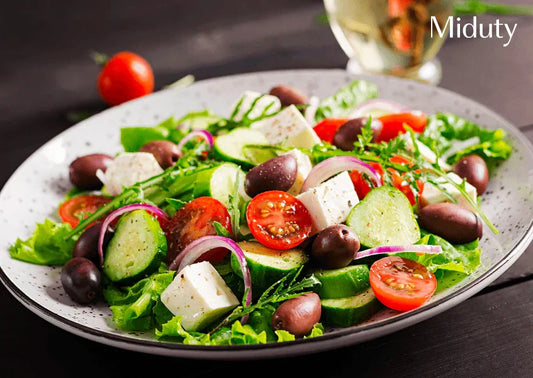 Colorful salad with cucumbers, tomatoes, olives, and feta cheese on a speckled plate