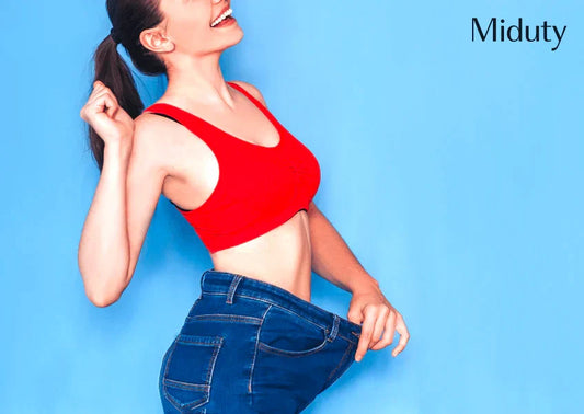 Woman in a red top smiling and holding out oversized jeans against a blue background