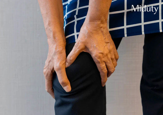 Person holding their knee with discomfort, wearing a blue and white patterned top