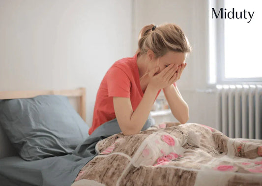 Woman sitting on a bed, covering her face with her hands, looking distressed
