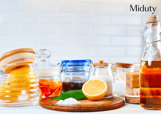 Variety of natural cleaning ingredients on a wooden countertop, including lemon, vinegar, and jars.