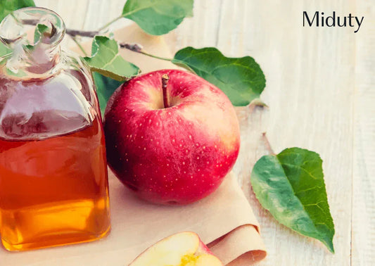Bottle of apple cider vinegar next to a red apple and green leaves on a wooden surface