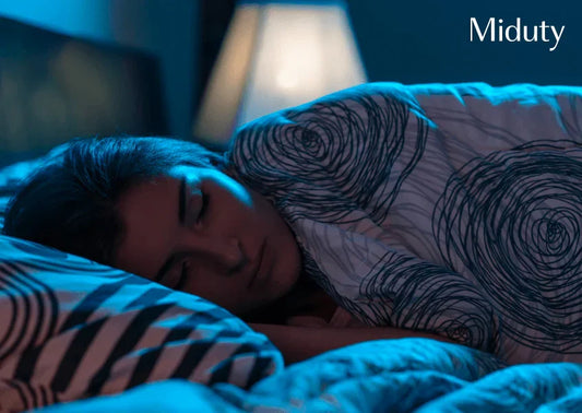 Person sleeping under a patterned blanket in a dimly lit bedroom