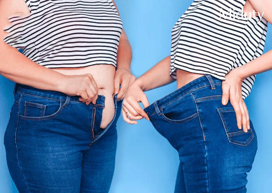 A woman showing a noticeable difference in waist size after weight loss in blue jeans.