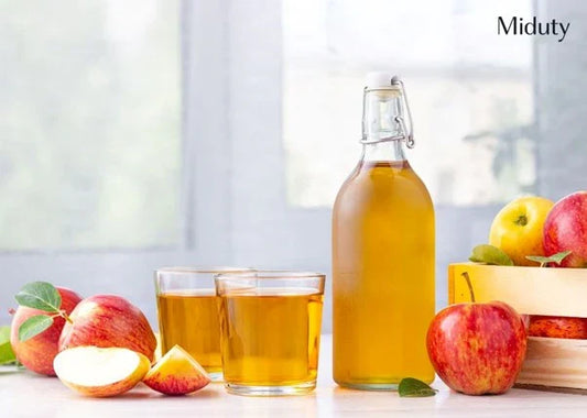 Bottle of apple cider vinegar with two glasses and fresh apples on a table